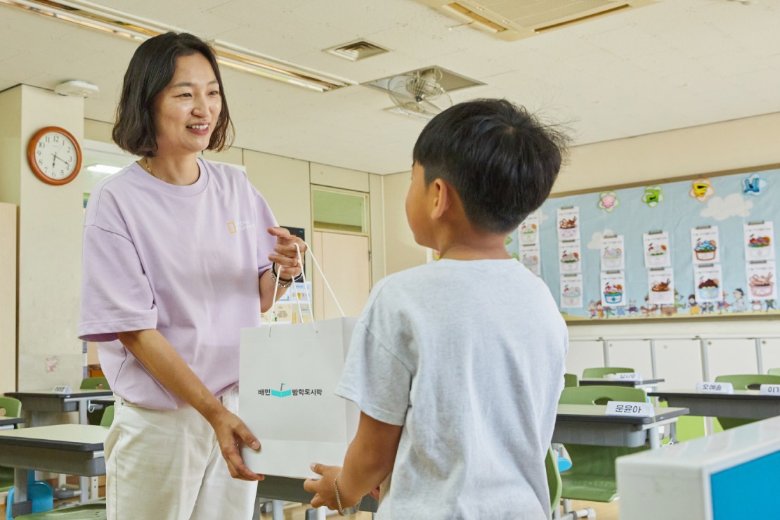 24년 배민여름방학도시락 사진(선생님이 아동에게 도시락을 전달하는 모습)